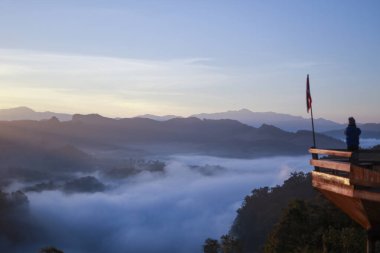 Huzurlu bir insan tek başına güzel dağ gündoğumunu seyrediyor. Sis kaplı manzara seyahat ve doğanın tadını çıkarmak için barışçıl bir manzara yaratır.