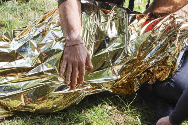 Altın sarısı acil durum battaniyesinin çimlerin üzerine yerleştirilmesi kurtarma durumundaki bakım ve güvenliği gösteriyor ve kazadan sonra hayatta kalmaya ve sıcaklığı korumaya odaklanıyor.