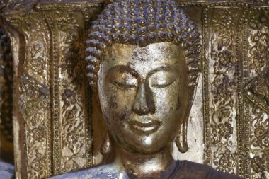Altın bronz Buda heykeli portresi huzur dolu sakin meditasyon yüzünü gözler kapalı antik oyma arka plan tapınağına karşı sergiliyor.