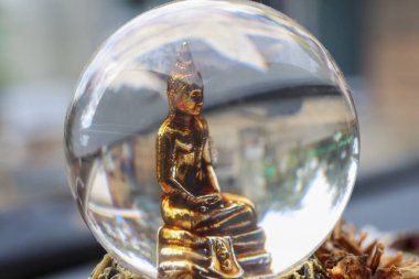 Altın Buda heykeli kristal merceğe baş aşağı yansıyor. Huzurlu meditasyon ifadesi, dışarıda, doğada gün ışığında kurutulmuş çam kozalağının üzerinde oturuyor.