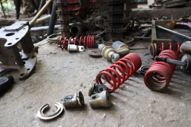 Parçalanmış kırmızı şok emici yaylar ve eski mekanik metal araç parçaları dağınık beton garaj zemini kirli endüstriyel bakım atmosferini ve tamir atölyesi konseptini gösteriyor.