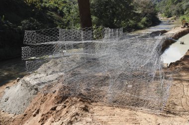 Büyük gabion örgüsü kafes inşaatı toprak erozyonunu koruyan nehir kıyısı orman akıntısı yakınlarındaki sel kontrolü için sağlam bir tasarım mühendislik ve endüstriyel konsept gösteriyor.