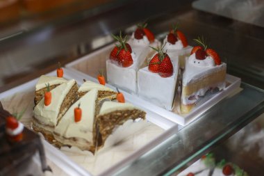 Lezzetli havuçlu kek dilimleri ve cam dolapta sergilenen çilekli kek tatlıya düşkün müşterileri yerel fırın kafeteryasında taze tatlı menüsüyle cezbediyor.