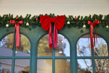 Şen yeşil kemerli pencere, canlı kırmızı kurdele, fiyonk ve beyaz balo süslemeleri, neşeli bayram ruhunu ve geleneksel Noel kutlamalarını çağrıştırıyor.