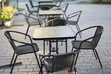 Siyah metal sandalyeler ve kare tabloların yer aldığı boş bir açık hava kafe verandası gri taş kaldırımda müşterilerin sabah yemeğinin keyfini çıkarmalarını bekliyor.