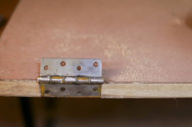 Endüstriyel dokuyu ve sağlam yapım detaylarını gösteren vidaları olan eskimiş kontrplak tahtasına bağlanmış paslı metal menteşenin yakın görüntüsü.