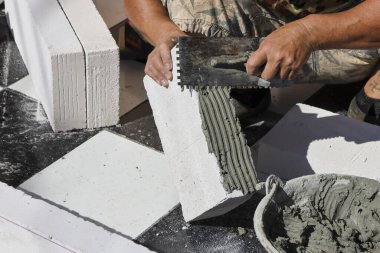 İnşaat işçisi elleri, ev yenileme işlemi sırasında beton bloğa çimento yapıştırıcı sürerek sağlam duvar yapısı oluşturur.