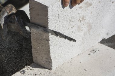 İnşaat işçisi, inşaat alanında profesyonel işçilik sergileyen duvar inşaatı için el testeresi ile otomatik klavsenli beton bloğu kesmeye odaklanmış.