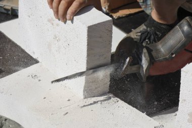 Odaklanmış tamirci, inşaat sahasında karşılıklı testere ile havalanan beton bloğu kesiyor. Ev yenileme için profesyonel elektrikli alet kullanarak kendini işe ve işçiliğe adadığını gösteriyor.