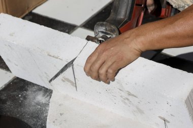 Odaklanmış inşaat işçisi otomatik klavsenli beton bloğu elektrikli öğütücü şantiyesiyle dikkatlice kesiyor. Açı kesici kullanarak duvar yapısı için beyaz tuğla şekillendiriyor.