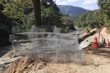 Gabion tel örgü sepetleri, doğada dayanıklılık ve yapısal bütünlüğü ifade eden orman manzarasında erozyon kontrolü ve duvar projesinin inşaatı için dağ yolunun yakınına istiflenmiştir.