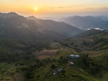 Dağlık arazide huzurlu bir gün doğumu sislerin ve sislerin arasından parlayan altın ışık huzmesi yeşil orman tepesi manzarası sakin ve sakin bir sabah atmosferi sunuyor.