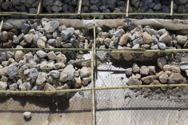 Yerdeki bambu çerçevesi tarafından organize edilmiş gri taş ve kaya yığınlarının yoğun endüstriyel duygu ve kaba dokularla oluşturulduğu bir inşaat alanı.