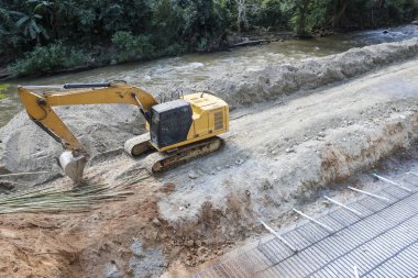 Sarı hidrolik kazıcı nehir kıyısı koruma şantiyesinde çalışıyor. Açık havada ağır makineler ile toprak ve toprak kazıyor.