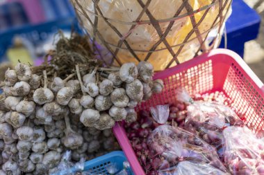 Köke bağlı çiğ organik sarımsak soğanları ve yerel Asya pazarında satılık pembe plastik sepette kırmızı soğan. Baharatlı yemek pişirmeye hazır taze ve aromatik malzemeler var.