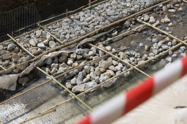 Gri taş ve kaya katmanlarını tutan güçlendirilmiş bambu ızgaralı yol ve nehir kıyısı şantiyesi güvenlik bölgesi için kırmızı beyaz uyarı bandı yakınlarında katı sanayi ilerlemesi gösteriyor.