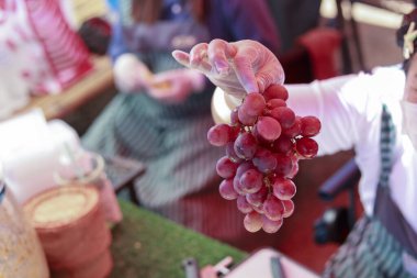 Satıcının elinde tuttuğu lezzetli kırmızı üzüm, yüksek kalitede organik tarım ürünlerini pazardaki tezgahta mutlu ve sağlıklı bir yaşam tarzı yiyeceği ile birlikte gösteriyor.