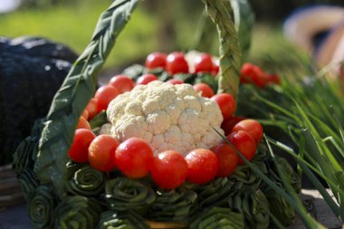 Taze çiğ karnabahar başı dokuma yeşil organik sepetin içinde oturmuş taze kiraz rengi domates halkası ve yeşil soğan yaprağı süslemesi güneşli bir günde mutluluk ve sağlıklı hasat duygularını gösteriyor.