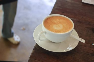Sıcak latte kahve fincanı ahşap masada, sıcak atmosferli, rahat ve huzurlu bir şekilde kahve dükkanında ya da restoranın arka planında birini bekliyor.
