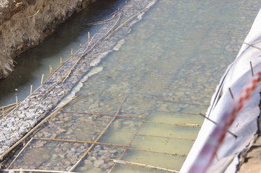 Yüksek açı görüntüsü, güçlendirilmiş çelik çubuk iskeleti ve bulanık suyla su basmış siperlerin durağan ilerlemeyi temsil eden terk edilmiş yol inşaatında karışıklığa yol açtığını gösteriyor.