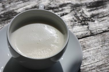 Bir fincan sıcak kahve sütlü latte beyaz seramik kupa kırsal gri ahşap masa açık kahve güneş ışığı, sıcak atmosfer içeceği, kahvaltı konsepti.