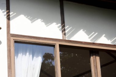 Çatı gölgesi olan beyaz duvar, Japon geleneksel ev mimarisinin ahşap pencere çerçevesinin üzerinde güneşli bir günde huzurlu, huzurlu ve duygusal bir atmosfer gösteriyor.