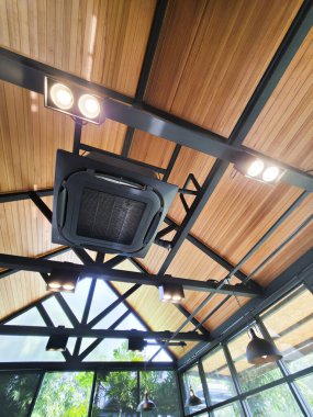 Ahşap panel ve siyah metal kiriş yapısı ile modern endüstriyel tavana bakarak ayrıntılı perspektif monte edilmiş ray ışığı ve merkezi kaset klima ünitesi ticari alan