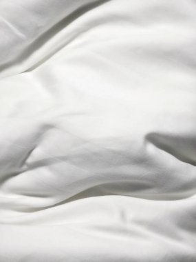Yumuşak kırışıklıkları ve dağınık kıvrımları olan temiz beyaz kumaş arka plan dokusu rahatlatıcı ve rahat bir yatak örtüsü ya da yatak odasındaki yorgan örtüsü hissi veriyor.