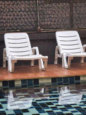 Havuz kenarında dinlenme havuzu atmosferi. İki boş plastik şezlong. Yüzme havuzunun sakin mavi sularında yaz tatilindeki konukları bekliyor.