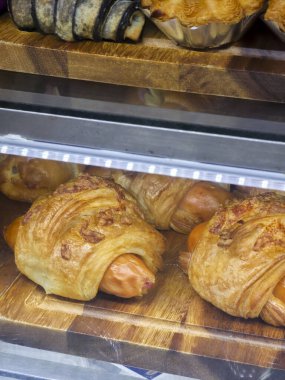 Fırında pişmiş sosisli puf böreği ahşap rafta, fırın vitrininde duruyor. Sıcak ışık, lezzetli kahverengi kabuğu aç müşteriler için hazır ve lezzetli atıştırmalıklar istiyor.