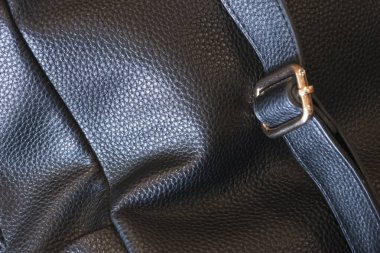 Zarif siyah deri çantanın yakın dokusunda kayış ve metal toka detaylı tahıl desenleri ve sağlam işçilik göstererek lüks ve sofistike moda aksesuarları yaratıyor.