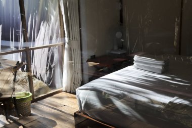 Huzurlu kırsal yatak odası. Rahat bir yatak odası ve beyaz havlu örtüsü istiflenmiş. Rahatlamayı güneşli doğa manzaralı pencereye davet ediyor.