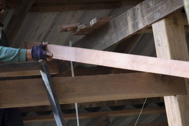 Düşük açılı marangoz eli koruyucu eldiven giyiyor. Uzun ahşap bir kalas tutuyor. Ev yenileme projesi için çatı kirişini dikkatlice yerleştiriyor.