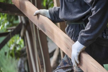 Usta marangozlar ağır ahşap kalaslar taşıyorlar. İnşaat sırasında çok dikkatli tutuyorlar. Koruyucu eldivenler giyiyorlar.