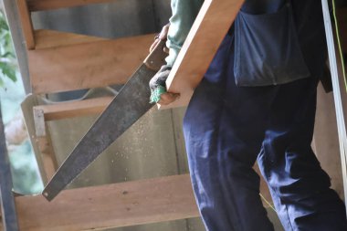 Ev yenileme projesi sırasında, omuz üzerinde kereste taşıyan ve kesin kararlılığı olan aktif inşaat işçisinin arkasını kapatın.