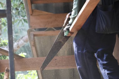 Odaklanmış profesyonel marangoz ağır ahşap kalas tutuyor. Emniyet eldiveni takıyor. Çerçeve yapısını özel kuvvetle inşa ediyor.