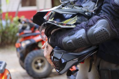 Koruyucu siyah motokros kaskı taşıyan sürücü, açık havada, kırmızı dörtlü bisiklet aracının yanında heyecanlı bir macera gezisi için heyecanlı bir şekilde aşırı spor hız yarışını bekliyor.