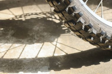 Açık hava tokmaklı motokros lastiğini kapatın. Beton zeminde güçlü gölgeler olsun. Maceracı, dayanıklı dokuyu ve güçlü tutuşu olsun.