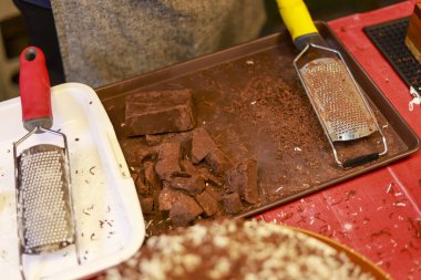 Ev yapımı hamur işi dekorasyonu için metal rendeleyici mutfak aletinin yanındaki dağınık tepside rendelenmiş çikolata parçacıkları ile tatlı tatlı hazırlama