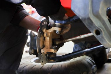 Tamirhanedeki araba süspansiyonunu tamir eden ayrıntılı tamirci el el frenleme diski ve atölyede görülebilen otomobil lastiği ile araç bakımı üzerine yoğunlaşmış profesyonel çalışmayı gösteriyor.