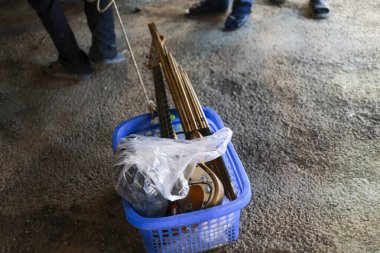 Kirli beton zemine yerleştirilmiş beyaz plastik çantalı, içinde ahşap ateşli tüfek veya el yapımı silah bulunan küçük mavi plastik sepet tehlikeli ve yasadışı bir atmosferi taşır.