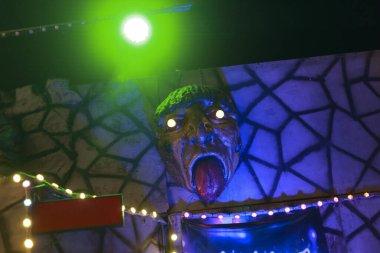 Ürkütücü cadılar bayramı dekorasyonu korkunç bir yüz ifadesi ve dili ile perili ev duvarları parlayan mor gece lambası karanlık atmosfer teması korkunç canavar kafası çılgın görünümlü