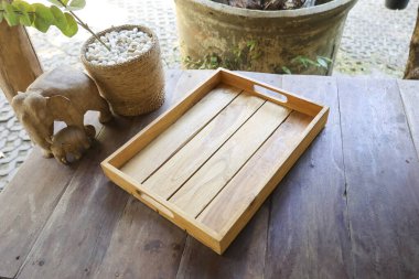 Boş ahşap tepsi kahverengi kırsal masa oyulmuş fil heykelinin yanında huzur dolu sakin bir ruh hali sergiliyor yiyecek içeceği kahvaltısı için mükemmel ya da ürün lokantası mutfağı ya da bahçe manzarası için.