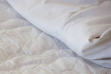 Yumuşak örtülü yatak koruyucu desenli temiz beyaz yatak katlanmış çarşafın altında huzurlu ve huzurlu bir atmosferi olan rahat bir uyku ortamı sunuyor.