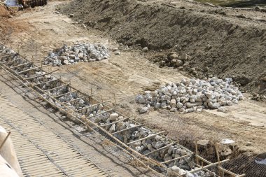 İnşaat sahasında çelik takviye çubukları ve hendekteki moloz yığınları, inşaat sürecinin kaotik ve ham gelişimini gösteren bir yapı çalışması