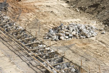 Metal inşaat demirinin içindeki sert taş malzemelerle birlikte inşaat alanı. Çerçeve yapısı, kuru kahverengi toprak zemini. Ağır endüstriyel mühendisliği gösteren inşaat alanı.