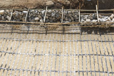 Zemin üzerinde kaya gabion sepeti ve çelik destek ızgarası bulunan eğim stabilizasyonunun yer aldığı inşaat alanı endüstriyel yapı sürecini gösteren somut çalışmalar için hazırlandı