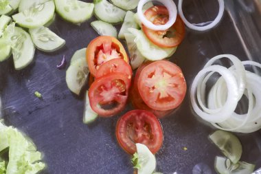 Taze kesilmiş sebze salatası, sağlıklı kırmızı domates, yeşil salatalık ve beyaz soğan halkaları, koyu tepside pişirilmek üzere hazır.
