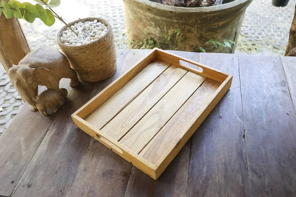 Boş ahşap tepsi kahverengi kırsal masa oyulmuş fil heykelinin yanında huzur dolu sakin bir ruh hali sergiliyor yiyecek içeceği kahvaltısı için mükemmel ya da ürün lokantası mutfağı ya da bahçe manzarası için.