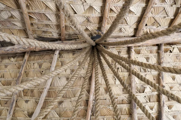 Geleneksel sazdan çatı yapısının alttaki görüntüsü, merkezi simetrik mimari desenden yayılan, arka plan ve kırsal kalın ip çizgilerini gösteren, kurutulmuş palmiye yaprağının güçlü dokusunu gösteriyor.
